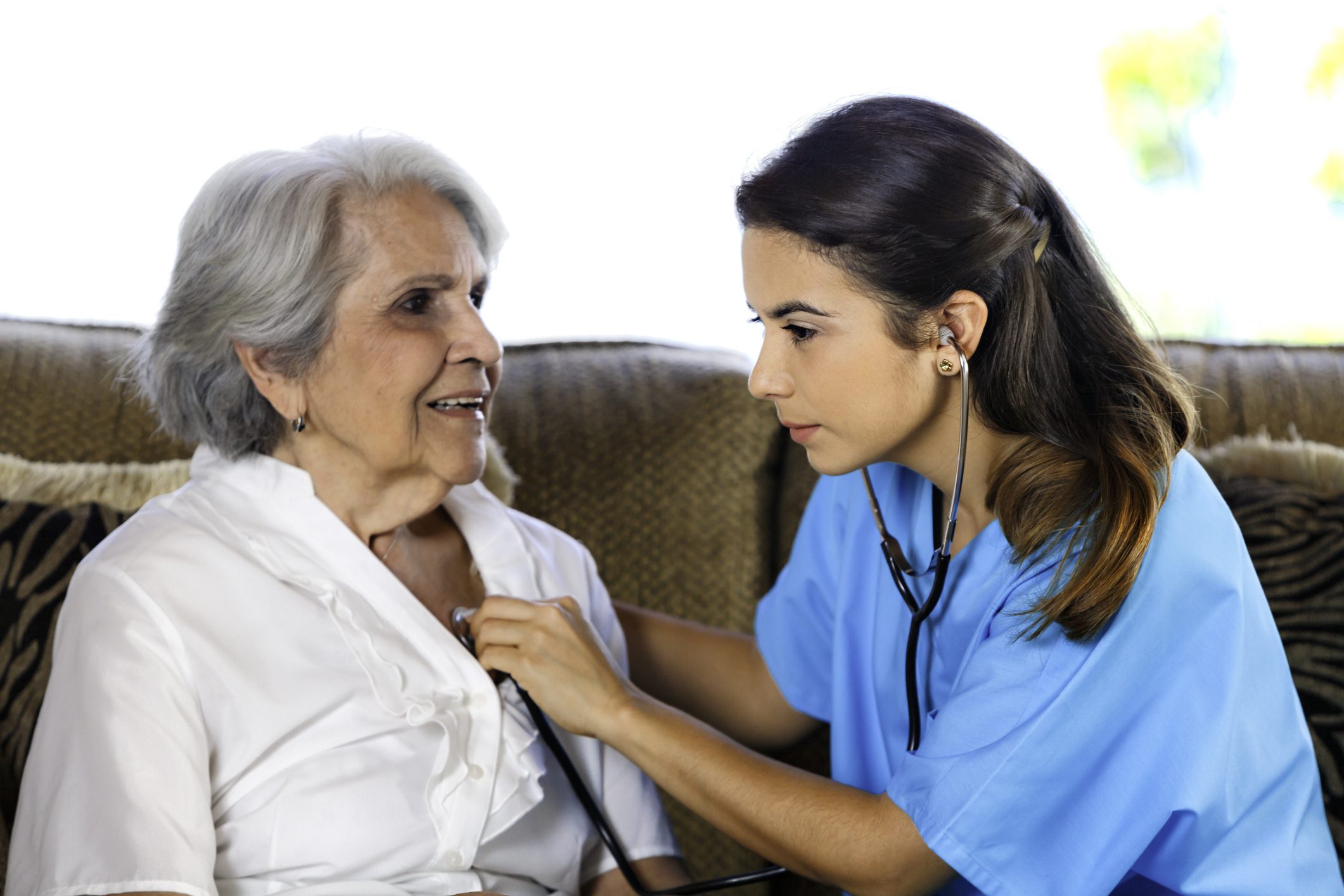 Nurse checking elderly woman's heartbeat with stethoscope.