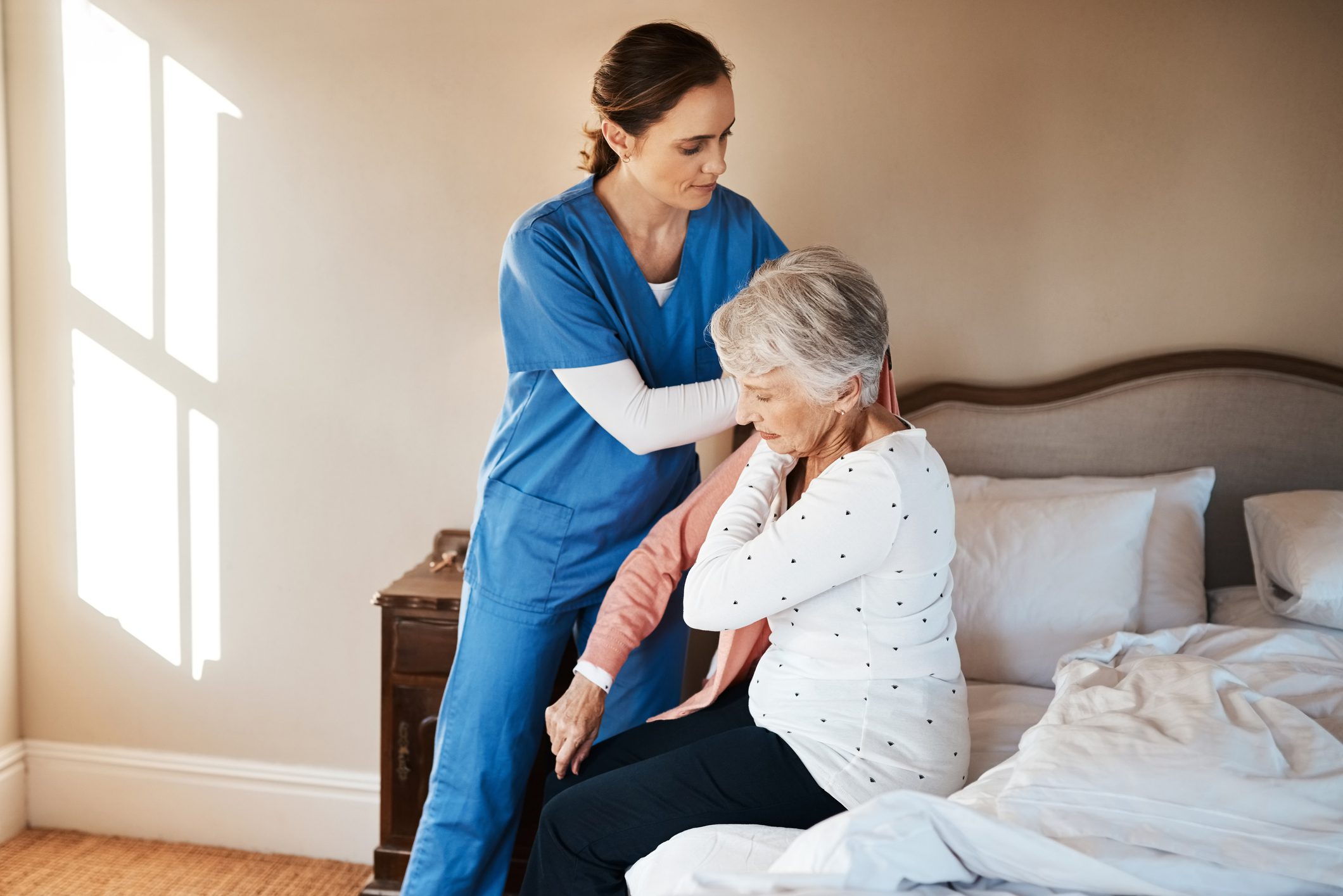 Caregiver assisting elderly woman on bed.