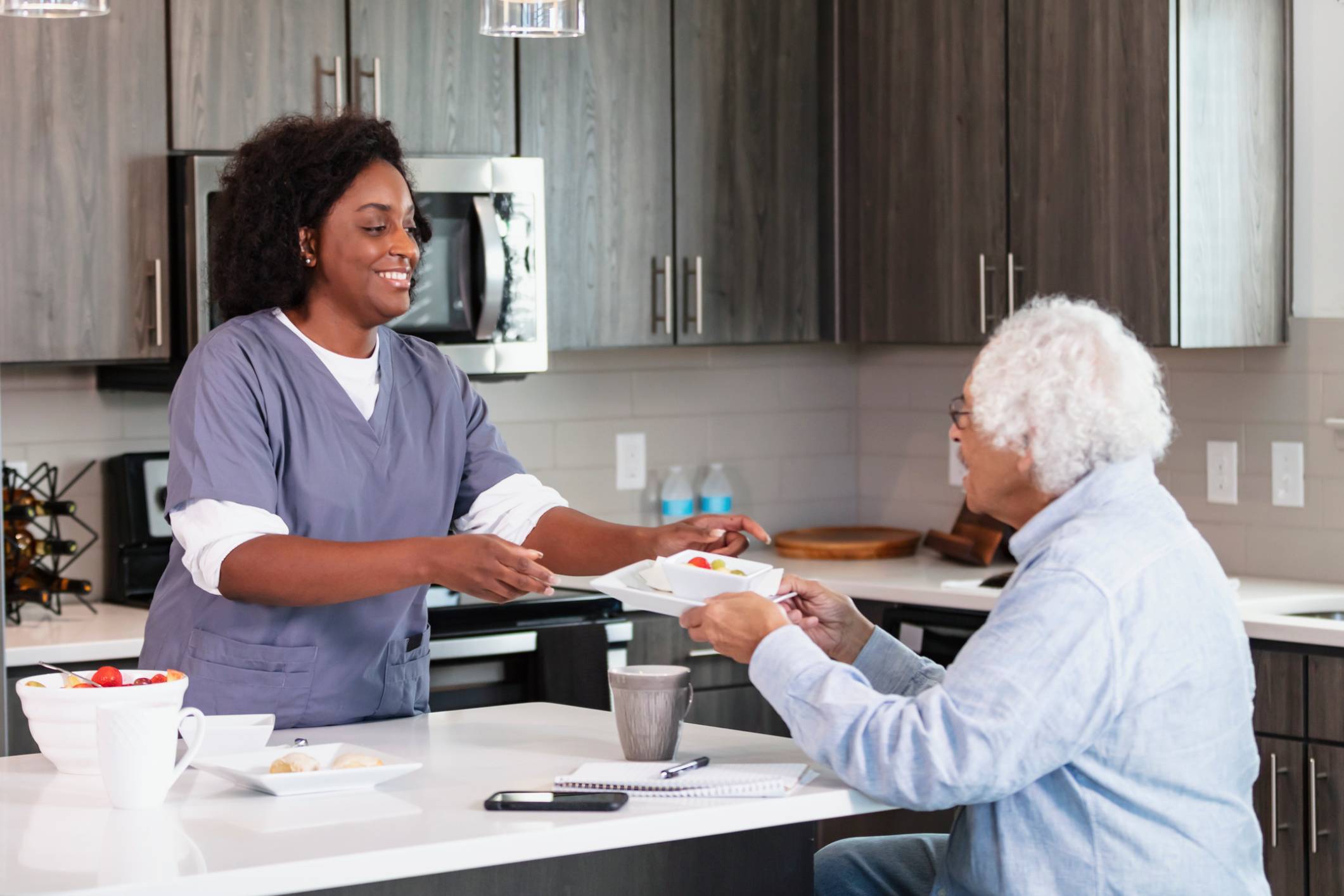 Caregiver serving meal to elderly person.