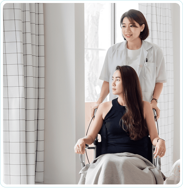 Woman in wheelchair with caring nurse nearby.